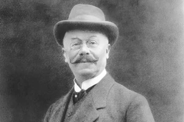     Ritratto di Emil Jellinek - in abito con gilet e camicia mentre fuma un sigaro, indossa un cappello rotondo, spiccano i suoi baffi caratteristici e il monocolo
